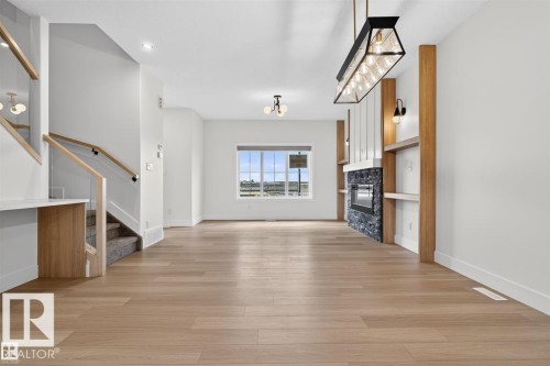 Expansive living space featuring light wood-finish flooring, a modern linear fireplace with dark stone surround, and built-in shelving with wood accents - 41 River Birch Way, St. Albert, AB 