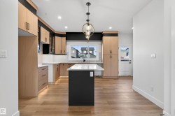 Open-concept kitchen featuring wood-finish flooring, a central island with a white countertop, two-tone cabinetry, recessed lighting, and a modern pendant light fixture - 