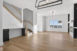 Bright open-concept living space with wood-finish flooring, a contemporary fireplace with a decorative tile surround, a large window, and a modern chandelier - 
