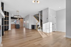 Open-concept living area featuring wide plank wood-finish flooring, a contemporary linear chandelier, and recessed lighting - 
