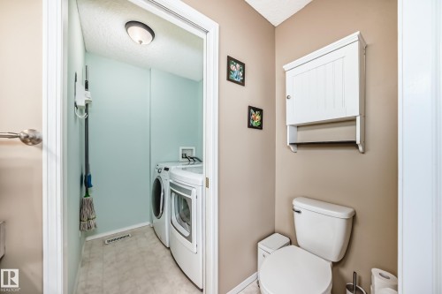 Dedicated laundry area featuring a stacked washer and dryer, complemented by a floor-mounted toilet, and wall-mounted storage cabinet - 11831 9 Avenue, Edmonton, AB 