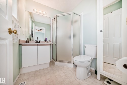 Bathroom featuring a white vanity with a neutral-toned countertop, a frameless mirror, a glass-enclosed shower, a white toilet, and patterned flooring - 11831 9 Avenue, Edmonton, AB 