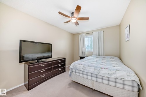 Bedroom featuring neutral wall paint, carpet flooring, a ceiling fan with integrated lighting, and a window with white curtains - 11831 9 Avenue, Edmonton, AB 