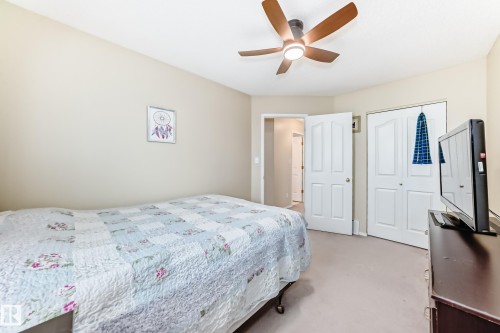 Bedroom featuring neutral wall paint, carpet flooring, a ceiling fan with integrated lighting, and white bi-fold closet doors - 11831 9 Avenue, Edmonton, AB 