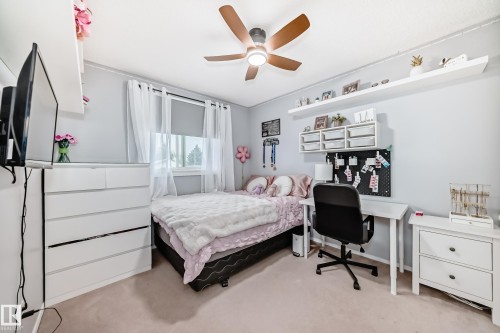 Bedroom featuring wood-finish ceiling fan with integrated lighting, wall-mounted shelving, built-in desk area, and window with roller shade - 11831 9 Avenue, Edmonton, AB 