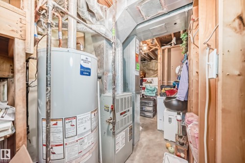 Utility area featuring a water heater, furnace, exposed ductwork, concrete flooring, and unfinished wood framing - 11831 9 Avenue, Edmonton, AB 