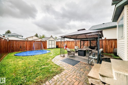 Expansive backyard featuring a red-toned privacy fence, a wooden deck with a gazebo, a brick paver patio, and a storage shed - 11831 9 Avenue, Edmonton, AB 