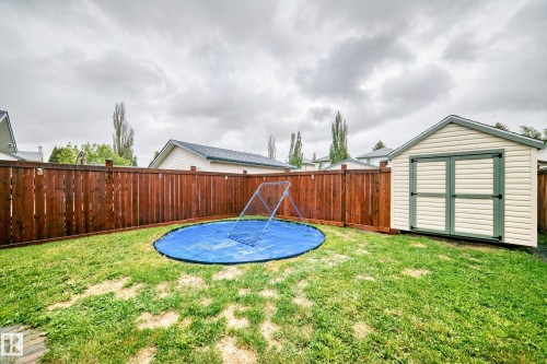 Private backyard featuring a freestanding storage shed with double doors, wood privacy fencing, and a grassy area - 11831 9 Avenue, Edmonton, AB 