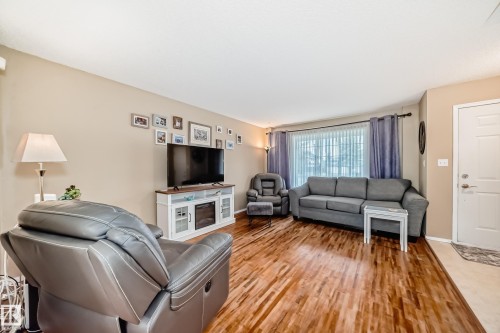 Living area featuring wood-finish flooring, neutral wall paint, and a large front-facing window - 11831 9 Avenue, Edmonton, AB 