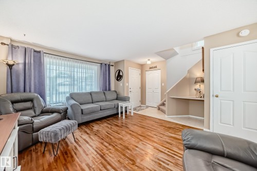 Spacious living area featuring wood-finish flooring, a large window with sheers, and neutral wall paint - 11831 9 Avenue, Edmonton, AB 