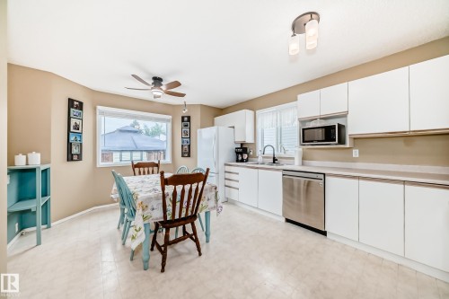 Kitchen and dining area featuring white cabinetry, stainless steel dishwasher, and a ceiling fan with integrated lighting - 11831 9 Avenue, Edmonton, AB 