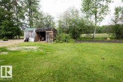Expansive lawn with mature perimeter trees, offering a rustic storage shed with an open bay and an enclosed screened section - 