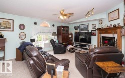 Living area featuring light-toned walls, carpet flooring, a ceiling fan with integrated lighting, and a prominent fireplace with a detailed wood mantel - 