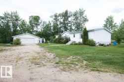 White-sided residence with an attached garage, featuring a gravel driveway and surrounding mature trees - 