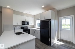 Modern kitchen featuring crisp white cabinetry, light-toned countertops, integrated sink with gooseneck faucet, black appliances, and a tiled backsplash - 