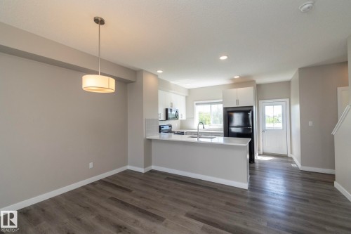 Open-concept kitchen and dining area featuring wood-finish flooring, white cabinetry, a kitchen island with seating, a stainless steel sink, and recessed lighting - 2610 Maple Way, Edmonton, AB 