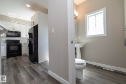 Kitchen and powder room featuring wood-finish flooring, white cabinetry, black appliances, a white pedestal sink, and a white toilet - 