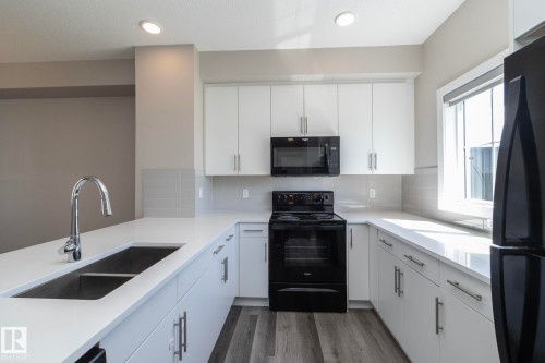 Kitchen featuring white cabinetry, light countertops, wood-finish flooring, and black appliances - 2610 Maple Way, Edmonton, AB 