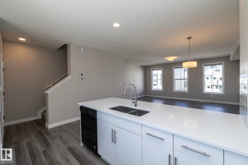 Kitchen island featuring a double basin sink with gooseneck faucet, white cabinetry, and integrated dishwasher - 2610 Maple Way, Edmonton, AB 
