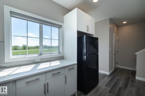 Kitchen area featuring a large window, light-toned cabinetry with contemporary hardware, a black refrigerator, and wood-finish flooring - 2610 Maple Way, Edmonton, AB 