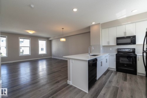 Open-concept living space featuring wood-finish flooring, a modern pendant light, and multiple windows - 2610 Maple Way, Edmonton, AB 