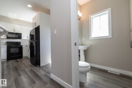 Kitchen and powder room featuring wood-finish flooring, white cabinetry, black appliances, a white pedestal sink, and a white toilet - 2610 Maple Way, Edmonton, AB 