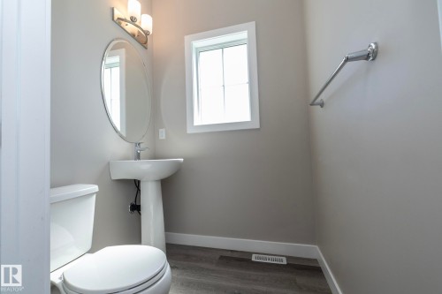 Pedestal sink with an oval mirror, complemented by a three-light vanity fixture - 2610 Maple Way, Edmonton, AB 