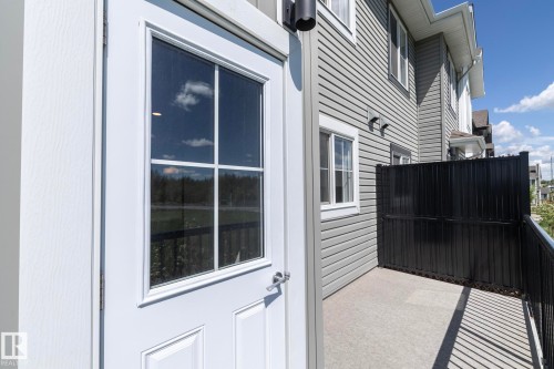 White paneled exterior door with divided light window, featuring a concrete patio, black metal privacy screen, and grey horizontal siding - 2610 Maple Way, Edmonton, AB 