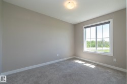 Neutral-toned room with a large grid-pane window, light grey carpeting, white baseboards, and a flush-mount ceiling light - 