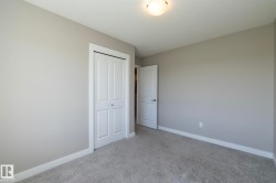 Neutral-toned room featuring a white bi-fold closet door, a white interior door, light grey carpeting, and white baseboards - 