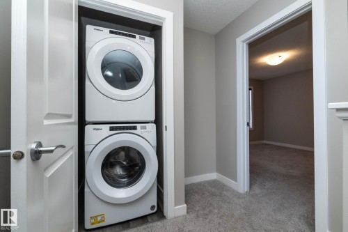 Integrated laundry closet featuring a stacked white washer and dryer, adjacent to a carpeted hallway with neutral wall tones - 2610 Maple Way, Edmonton, AB 