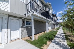 Contemporary townhouse exterior featuring light grey siding, a white front entry door, and a private upper-level balcony with a black railing - 