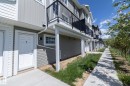 Contemporary townhouse exterior featuring light grey siding, a white front entry door, and a private upper-level balcony with a black railing - 2610 Maple Way, Edmonton, AB 