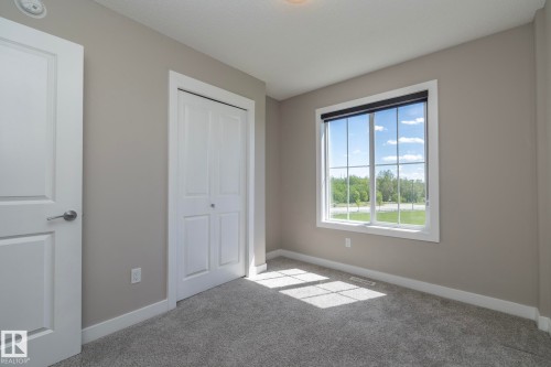 Room featuring a large window with white muntins, neutral gray wall paint, white baseboards, and gray carpeting - 2610 Maple Way, Edmonton, AB 