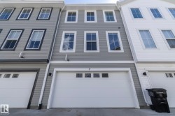 Three-story townhome exterior featuring gray horizontal siding and a white garage door with upper window panels - 