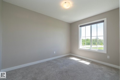 Neutral-toned room with a large grid-pane window, light grey carpeting, white baseboards, and a flush-mount ceiling light - 2610 Maple Way, Edmonton, AB 
