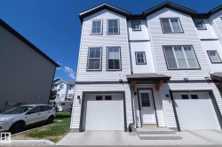 Modern townhome exterior featuring white horizontal siding, dark trim, multiple windows, a covered entry, and an integrated garage - 