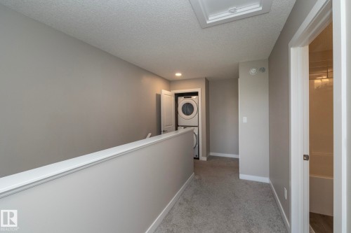 Upper-level laundry area featuring stacked appliances, a gray carpeted floor, and neutral gray wall paint - 2610 Maple Way, Edmonton, AB 