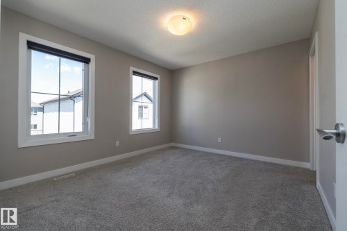 Spacious room featuring neutral paint, gray carpeting, dual windows with white trim, and a contemporary ceiling light fixture - 2610 Maple Way, Edmonton, AB 