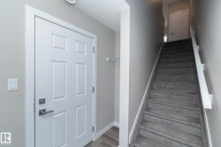 Entryway featuring a paneled door with brushed nickel hardware, light gray walls, wood-finish flooring, and a carpeted staircase with white railings - 