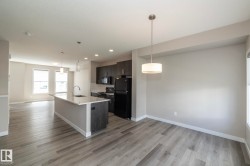 Open-concept living area with light wood-finish flooring, a kitchen island featuring a waterfall countertop and undermount sink, dark wood cabinetry, and a black appliance suite - 