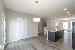 Spacious interior featuring wood-finish flooring, a kitchen island with a built-in sink and pendant lighting, recessed ceiling lighting, and multiple windows providing ambient light - 