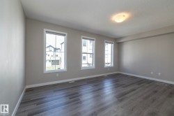 Spacious room featuring three large windows with white trim, wood-finish flooring, a neutral wall palette, and a semi-flush mount ceiling light fixture - 