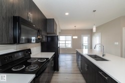 Modern kitchen featuring dark wood-finish cabinetry, white countertops, and a full suite of black appliances - 
