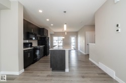 Modern kitchen featuring dark wood-finish cabinetry, black appliances, subway tile backsplash, and a central island with a light-toned countertop - 