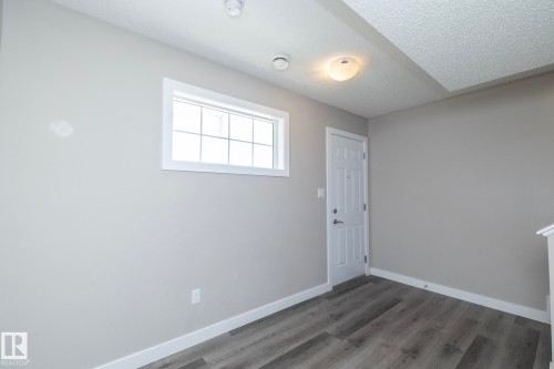 Bright room with light gray walls, wood-finish flooring, a white paneled door, and a multi-pane window - 2610 Maple Way, Edmonton, AB 