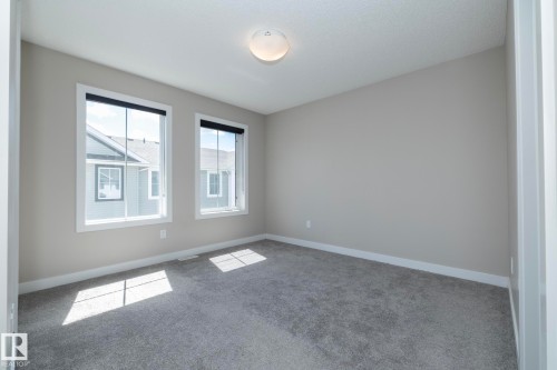 Neutral-toned room featuring a light grey carpet, two windows with black roller blinds, and white trim - 2610 Maple Way, Edmonton, AB 
