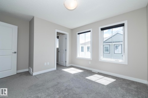Spacious room featuring neutral painted walls, two windows with black roller shades, white trim, and light gray carpeting - 2610 Maple Way, Edmonton, AB 