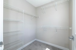 Walk-in closet featuring light gray wall paint, white wire shelving, white baseboards, and gray carpet flooring - 