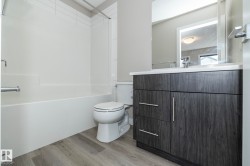 Bathroom featuring a dark wood-finish vanity with a white countertop and rectangular sink, a white bathtub with a tiled surround, and wood-finish flooring - 